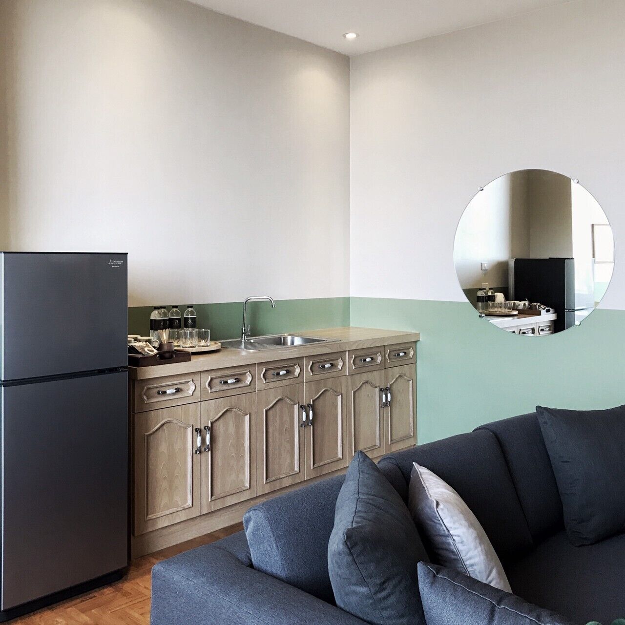 A modern kitchen with a black refrigerator, wooden cabinets, and a green accent wall.