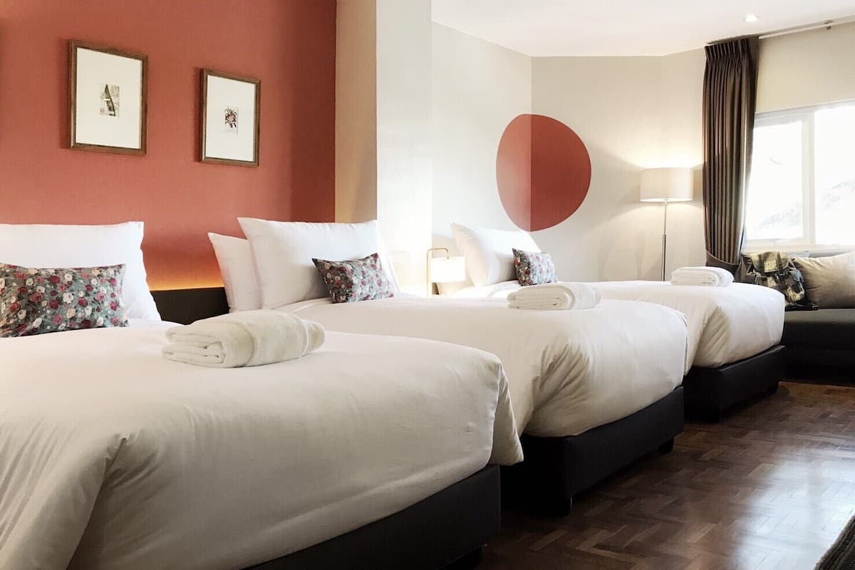 Hotellihuone, jossa on kolme sänkyä, suuri ikkuna, jossa on verhot, ja yksi seinä on maalattu punaisella.