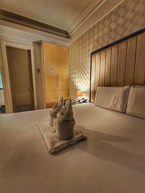 A hotel room with a large bed, a wooden wardrobe, a nightstand with a lamp, and a door with a sign. - S&M Hotel (Mandaue)