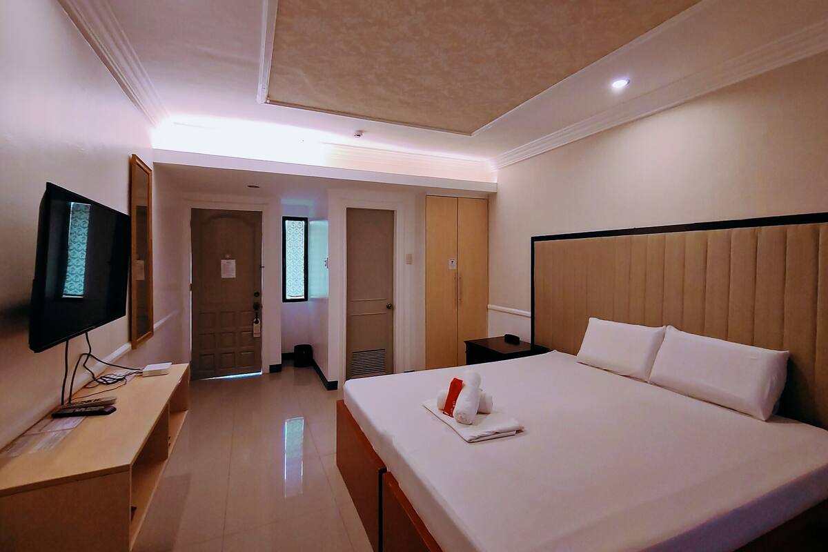 Quarto de hotel com cama, televisão, secretária e armário.