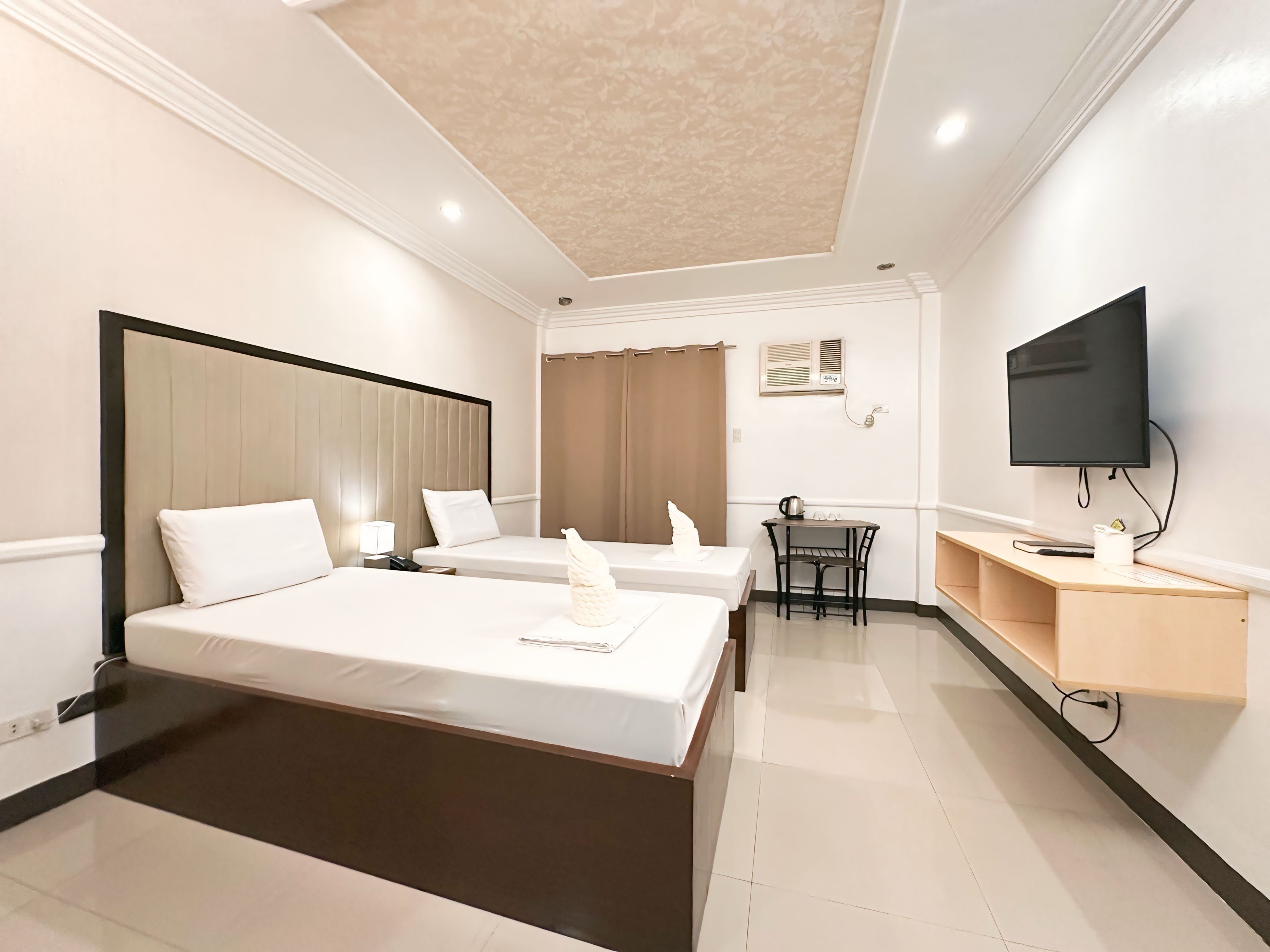 A hotel room with two beds, a desk, a television, and a ceiling fan.