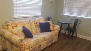 Una habitación con un sofá estampado, dos cojines azules, una mesita redonda y dos sillas.