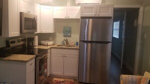Una cocina compacta con armarios blancos, un refrigerador de acero inoxidable, un microondas y un tostador.