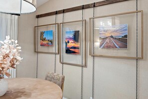 Zona pranzo con tavolo e sedie, un vaso con fiori secchi e tre quadri appesi al muro.