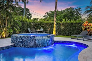 A swimming pool with a mosaic edge, surrounded by greenery and a sunset sky.