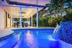 A swimming pool with a waterfall feature, surrounded by a covered patio area with seating.