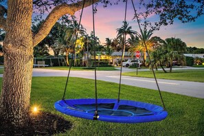 Un trampolino sotto un albero in un quartiere residenziale, con case e un segnale di stop sullo sfondo.