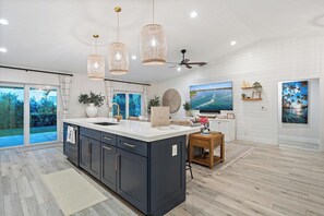 A modern kitchen with a large island, pendant lights, and a ceiling fan.
