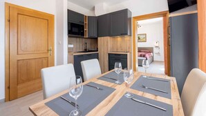 Une cuisine moderne avec des meubles de couleur sombre, un four à micro-ondes et un coin repas doté d’une table en bois, dressée pour quatre personnes.