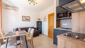 Une cuisine moderne équipée d’un four à micro-ondes, d’une cuisinière et de meubles de rangement en bois. On y trouve un coin repas avec une table et des chaises, ainsi qu’un canapé à l’arrière-plan.