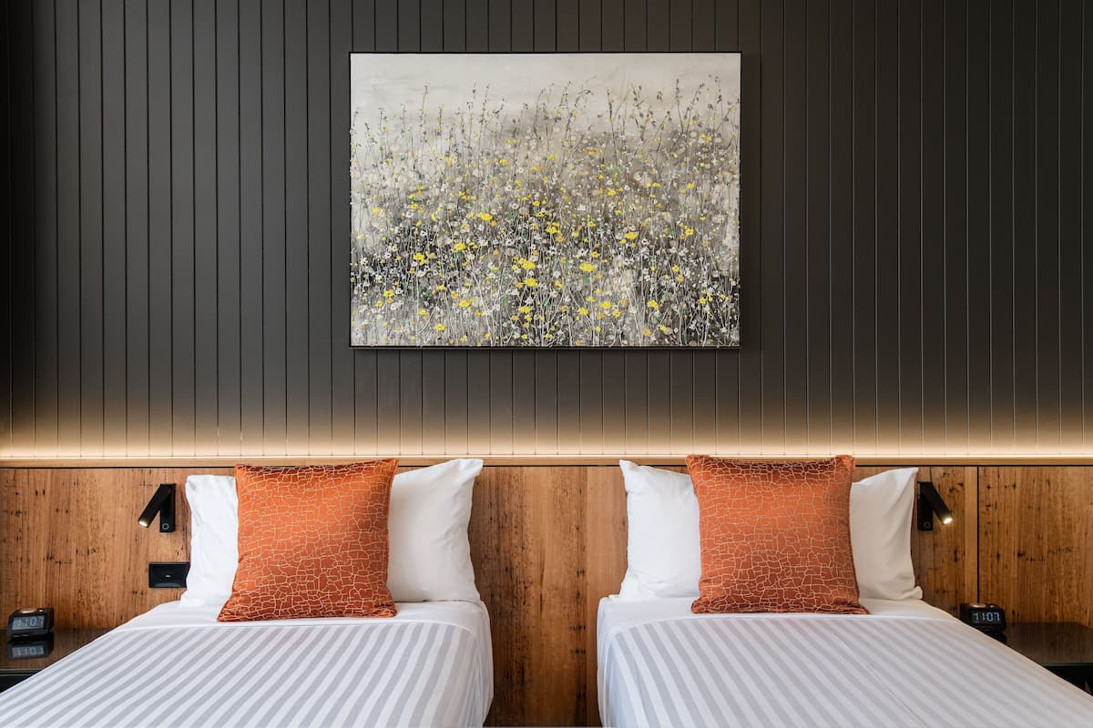 A modern hotel room with two beds, wooden headboard, and a large abstract painting on the wall.