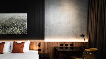 A hotel room with a bed, a desk, a chair, a lamp, and a large abstract painting on the wall.