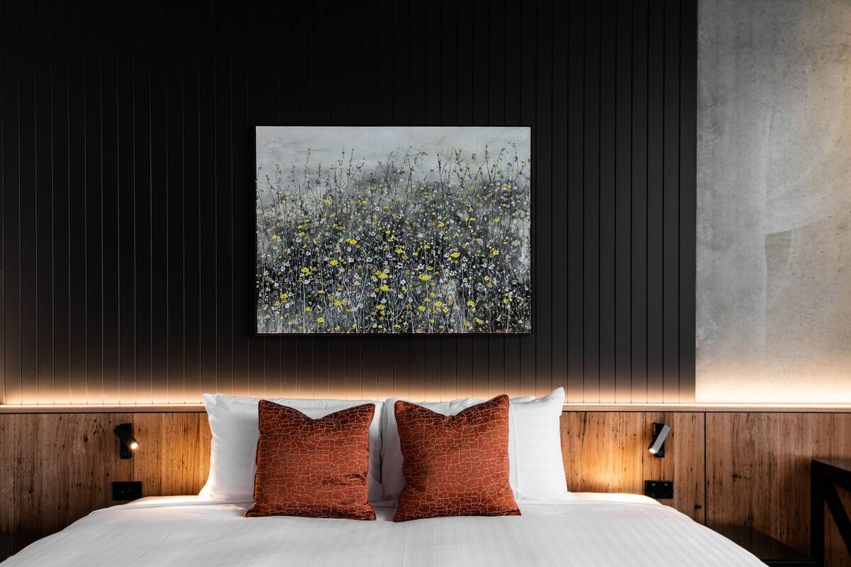 A modern hotel room with a large bed, two decorative pillows, a wall-mounted artwork, and a wooden panel design.