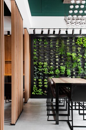 Un espace de restauration moderne avec une longue table, des chaises noires et un mur végétal vertical.