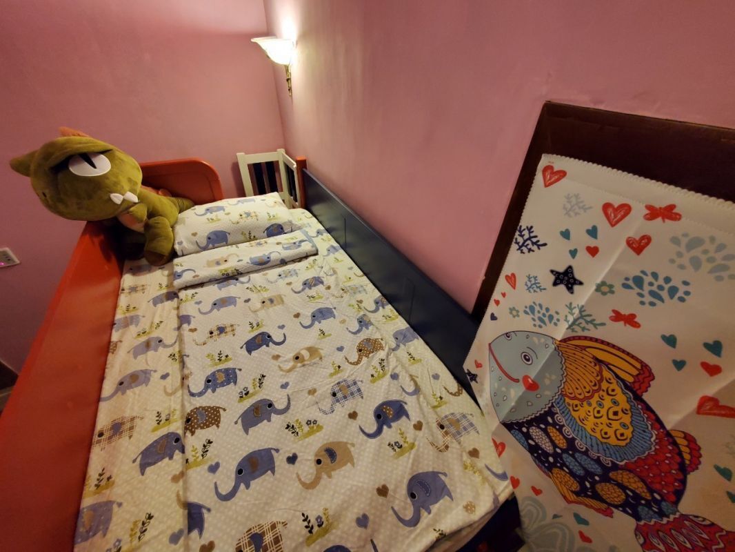 Uma cama de criança com um cobertor estampado, um brinquedo de pelúcia e um travesseiro decorativo.