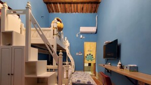 Una cama litera para niños con escritorio y silla, un televisor y una pequeña estantería con adornos.