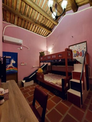 A room with a bunk bed, a desk, a chair, a poster, and a ceiling fan.