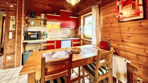 A wooden cabin interior with a kitchen, dining table, chairs, and a window with curtains. - Schöne Aussicht by Interhome (Adenau)