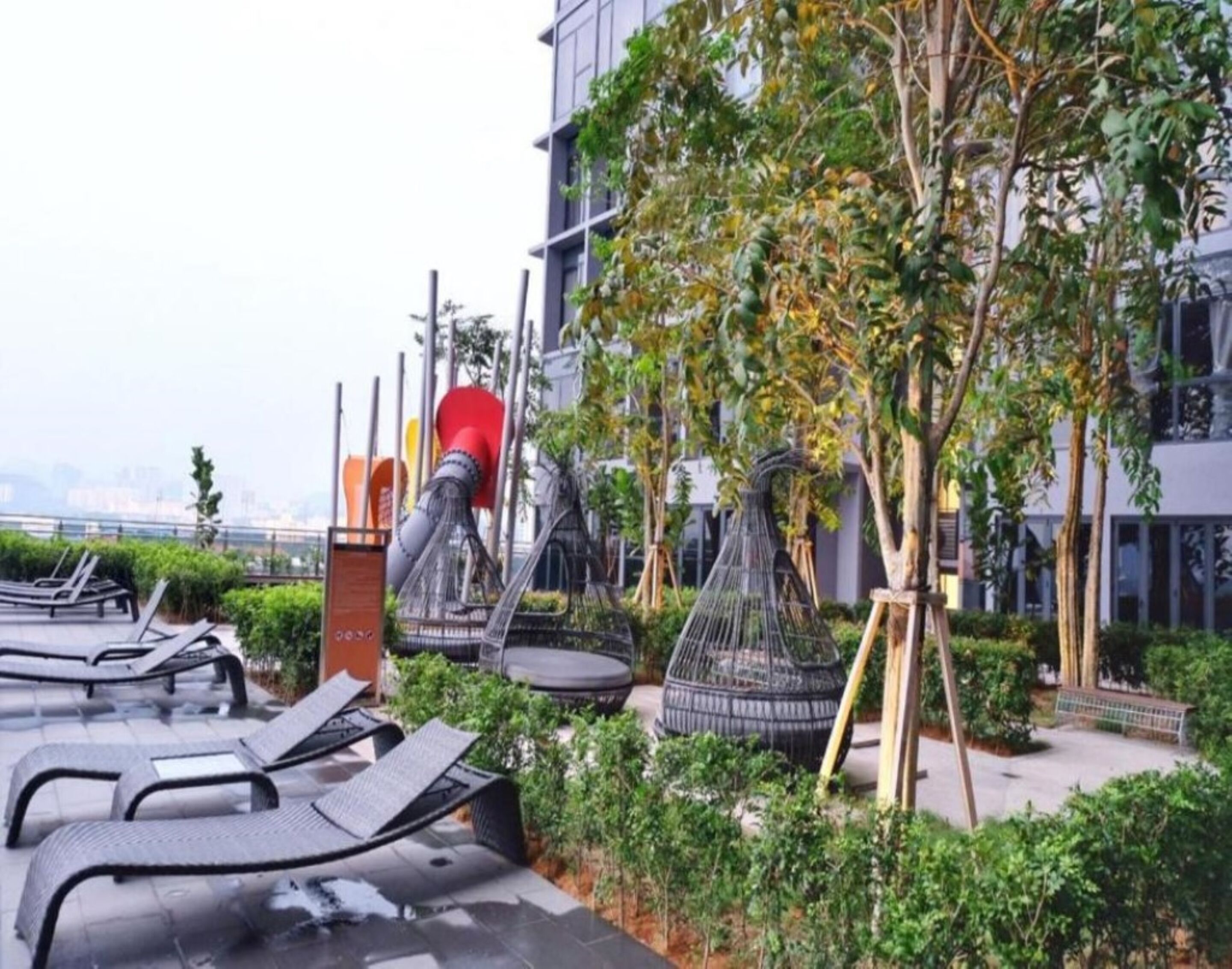 Un jardín en la azotea con sillones de descanso, un tobogán rojo y una jaula para pájaros.