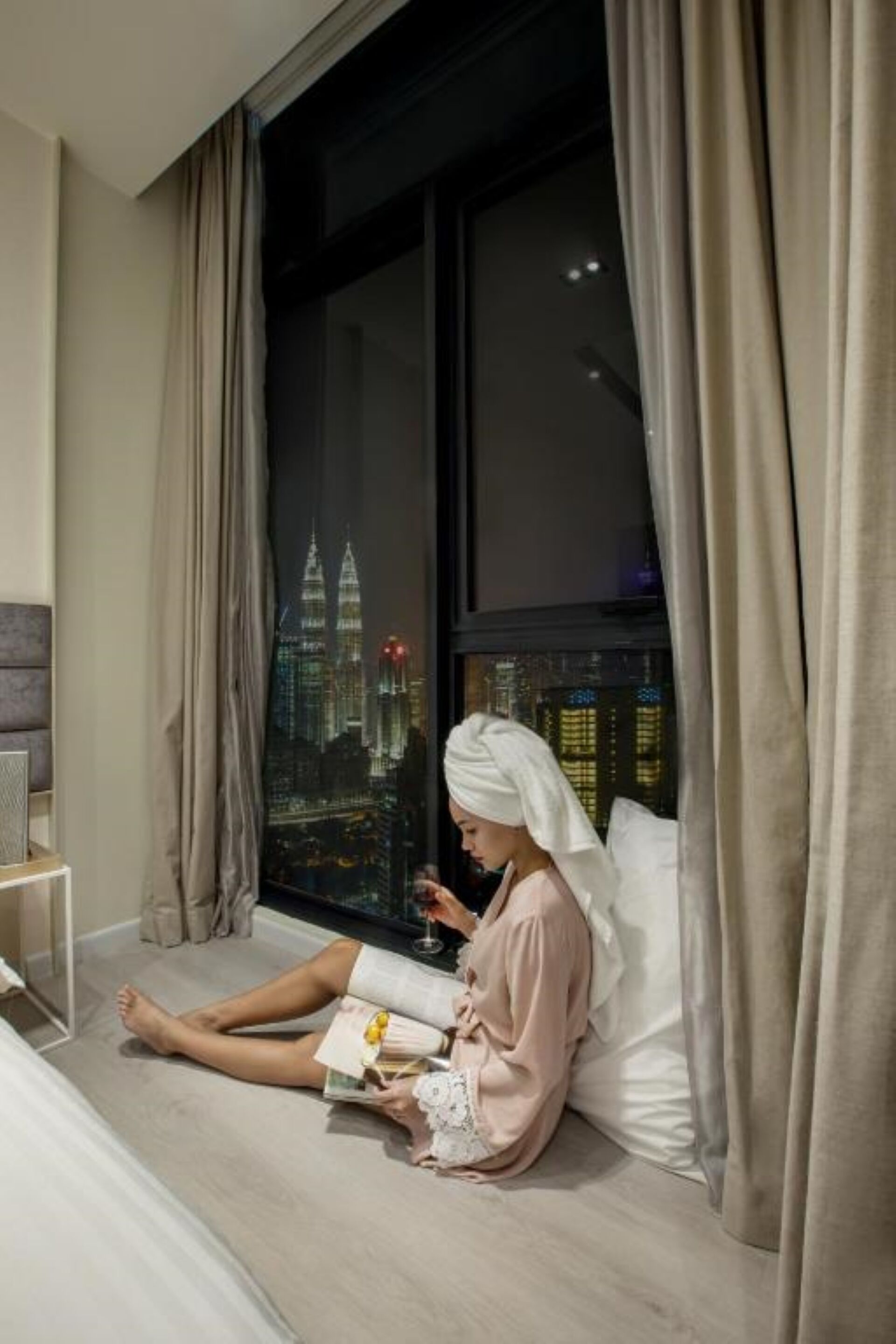 A person sitting by a window with a cityscape view, reading a book.