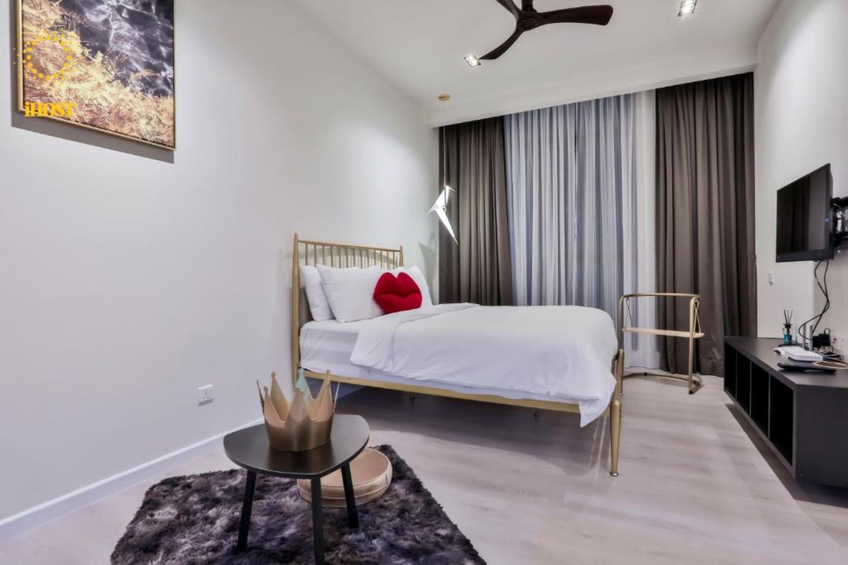 A modern bedroom with a bed, a small table, a TV, and a large window with curtains.