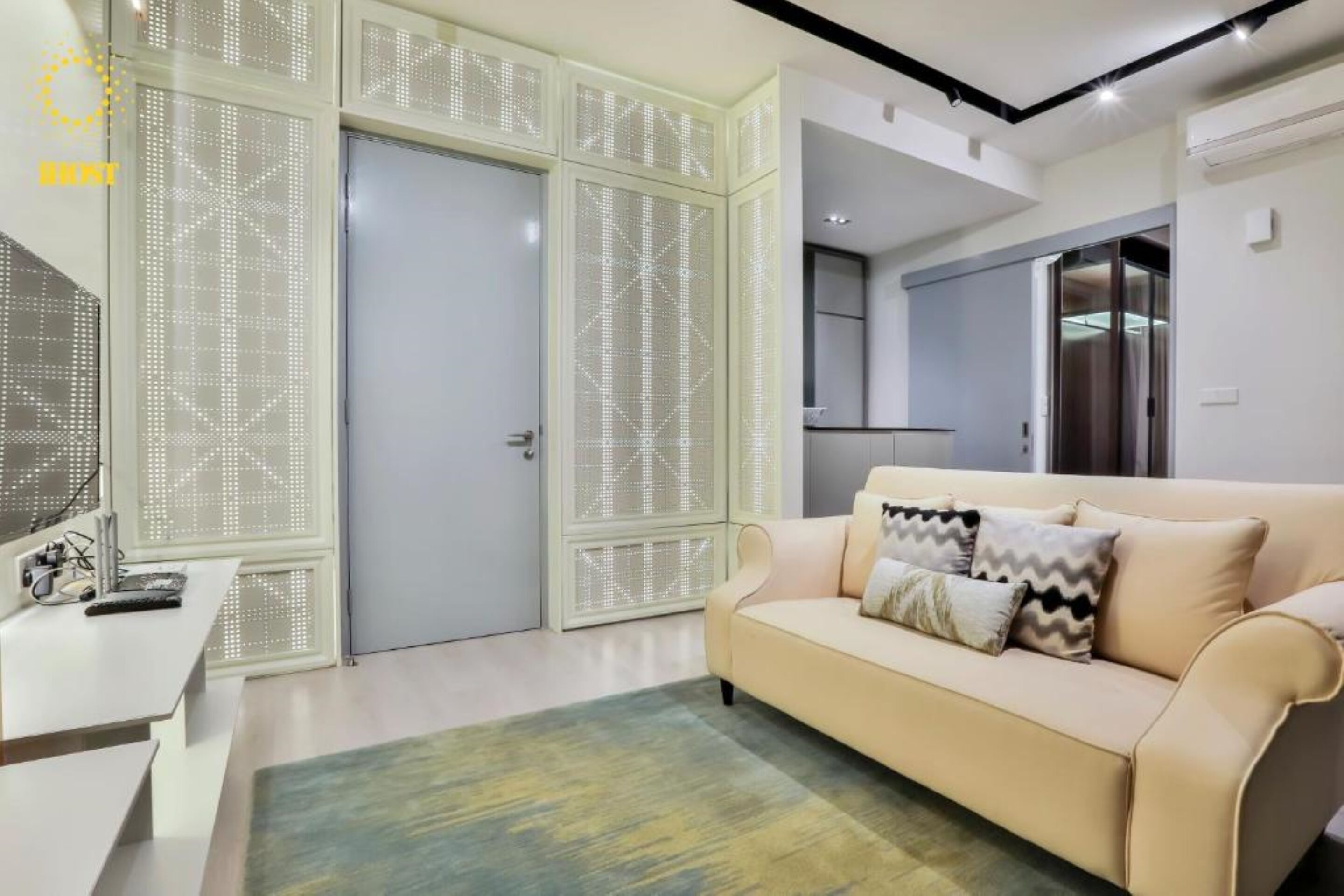 Un salon moderne avec un canapé beige, un tapis à motifs et un meuble blanc au design géométrique.
