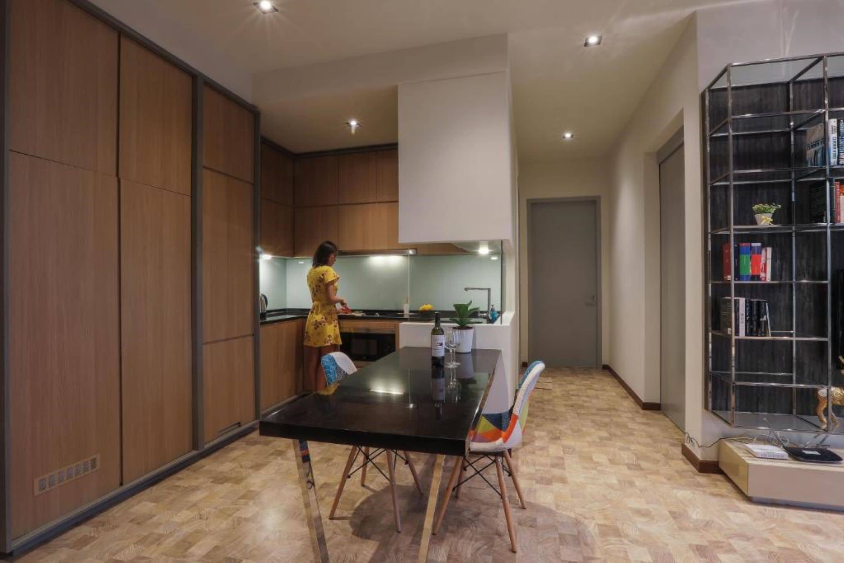 A modern kitchen with wooden cabinets, a black dining table, and a bookshelf.