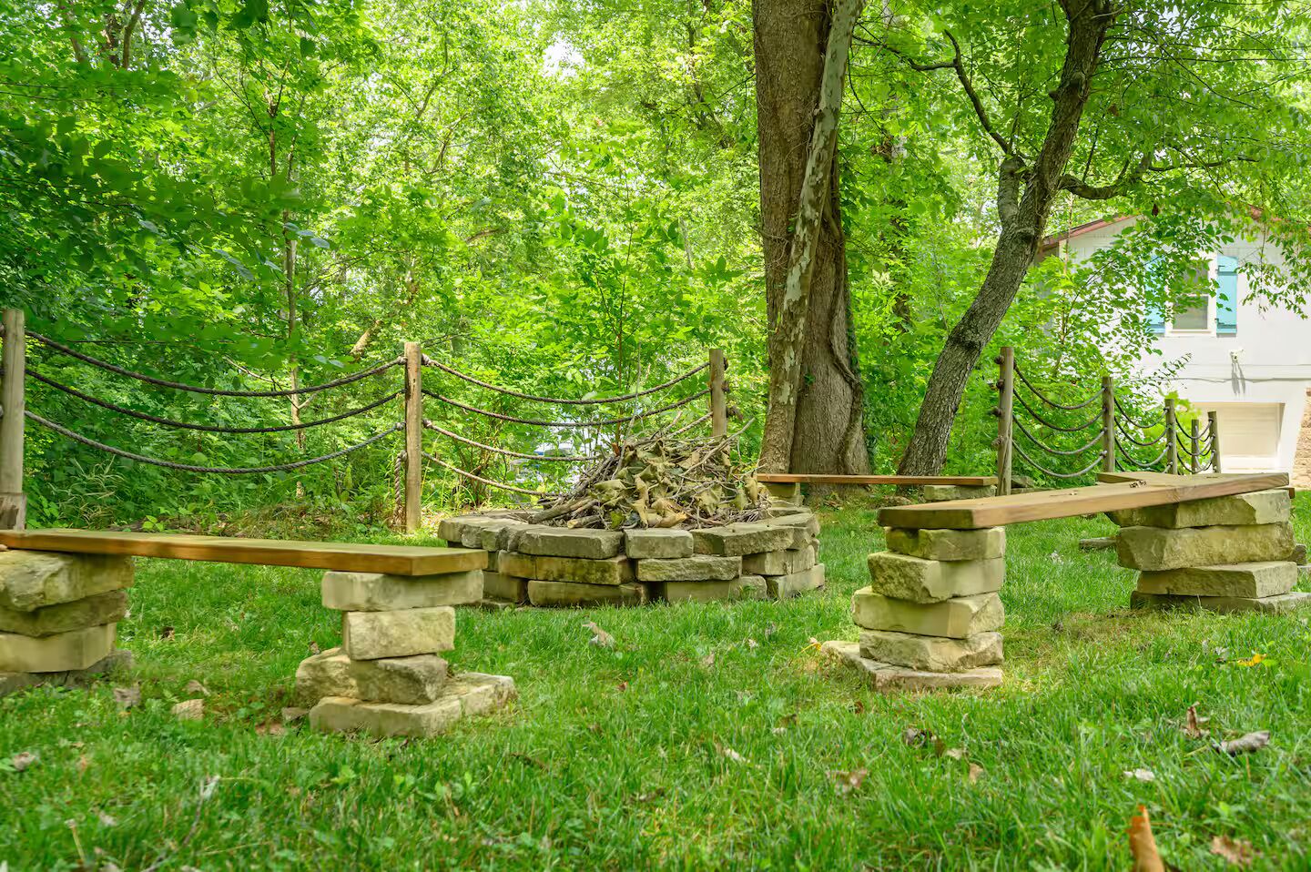 A rustic outdoor area with stone benches and a rope barrier, surrounded by lush greenery.
