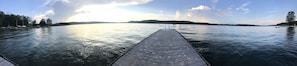 A wooden pier extending into calm water with a distant shoreline and trees.