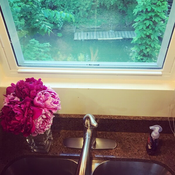 A kitchen with a window, a sink, a faucet, and a vase of flowers on the counter.