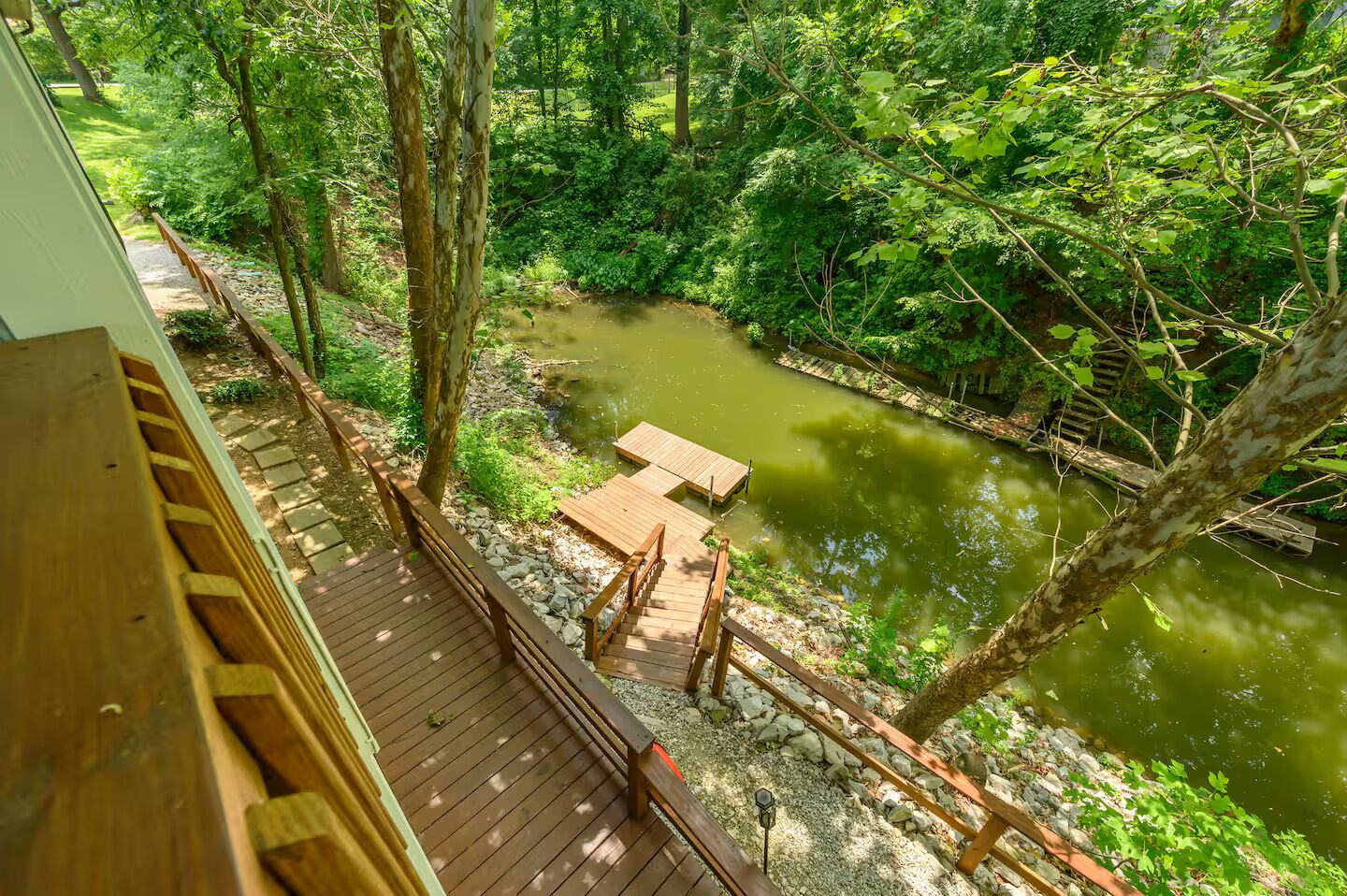 A wooden deck overlooking a river with a wooden bridge and benches.