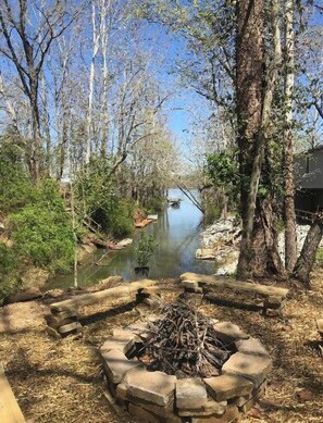A riverside campsite with a fire pit and a boat on the water.