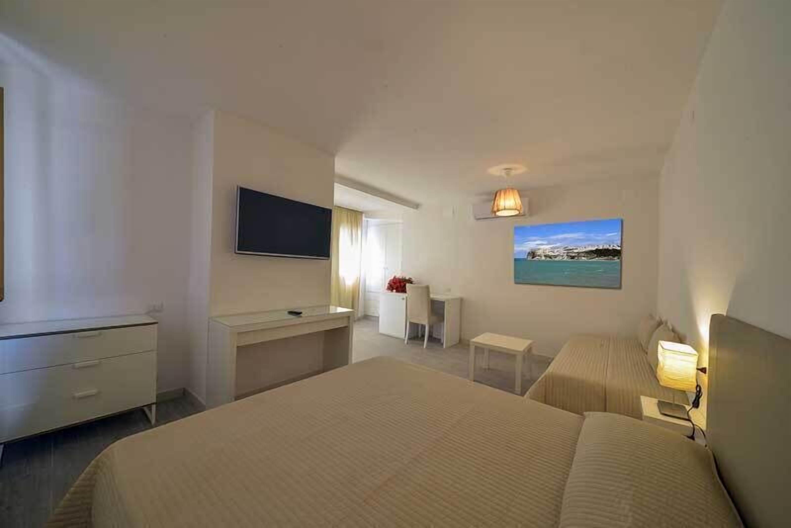 A hotel room with a large bed, a desk, a chair, a TV, and a painting of a landscape.
