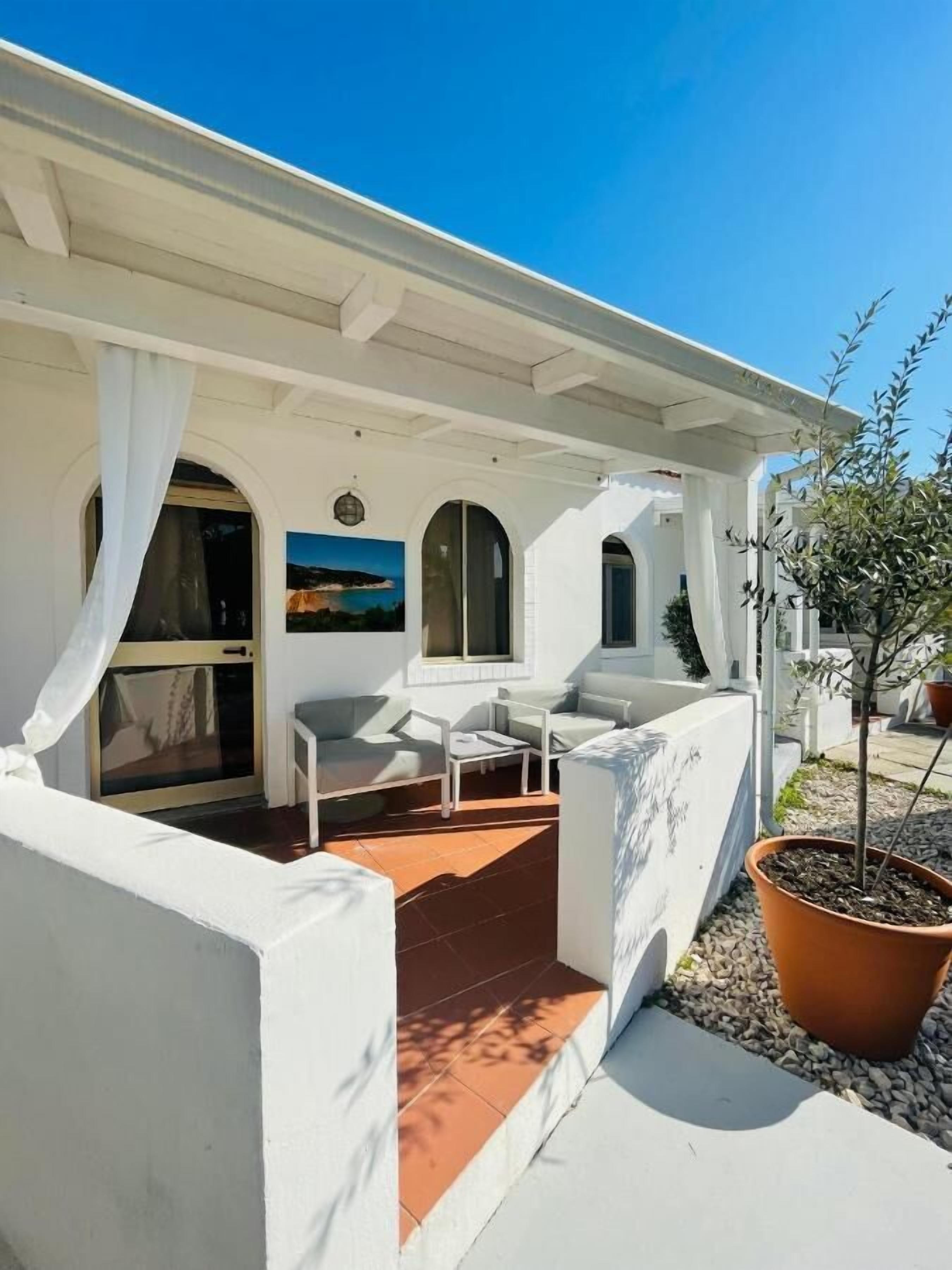 Un edificio blanco con un patio cubierto, mobiliario exterior y una planta en maceta.