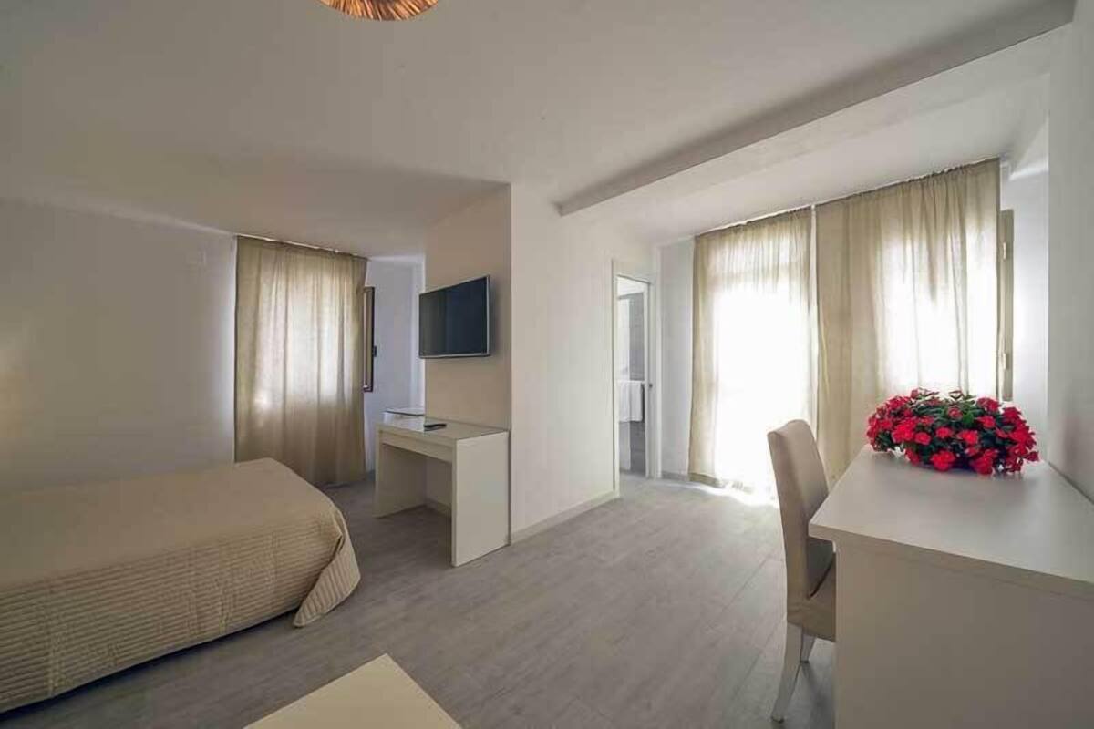A hotel room with a bed, a desk, a chair, a TV, and a window with curtains.