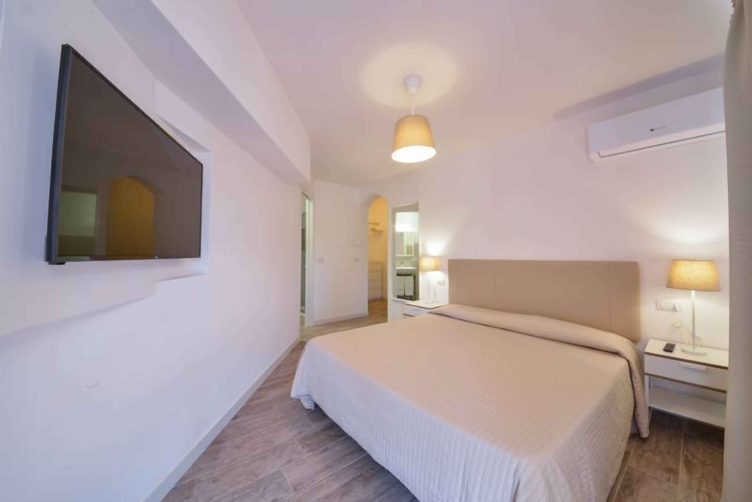A hotel room with a bed, bedside table, lamp, and a TV mounted on the wall.