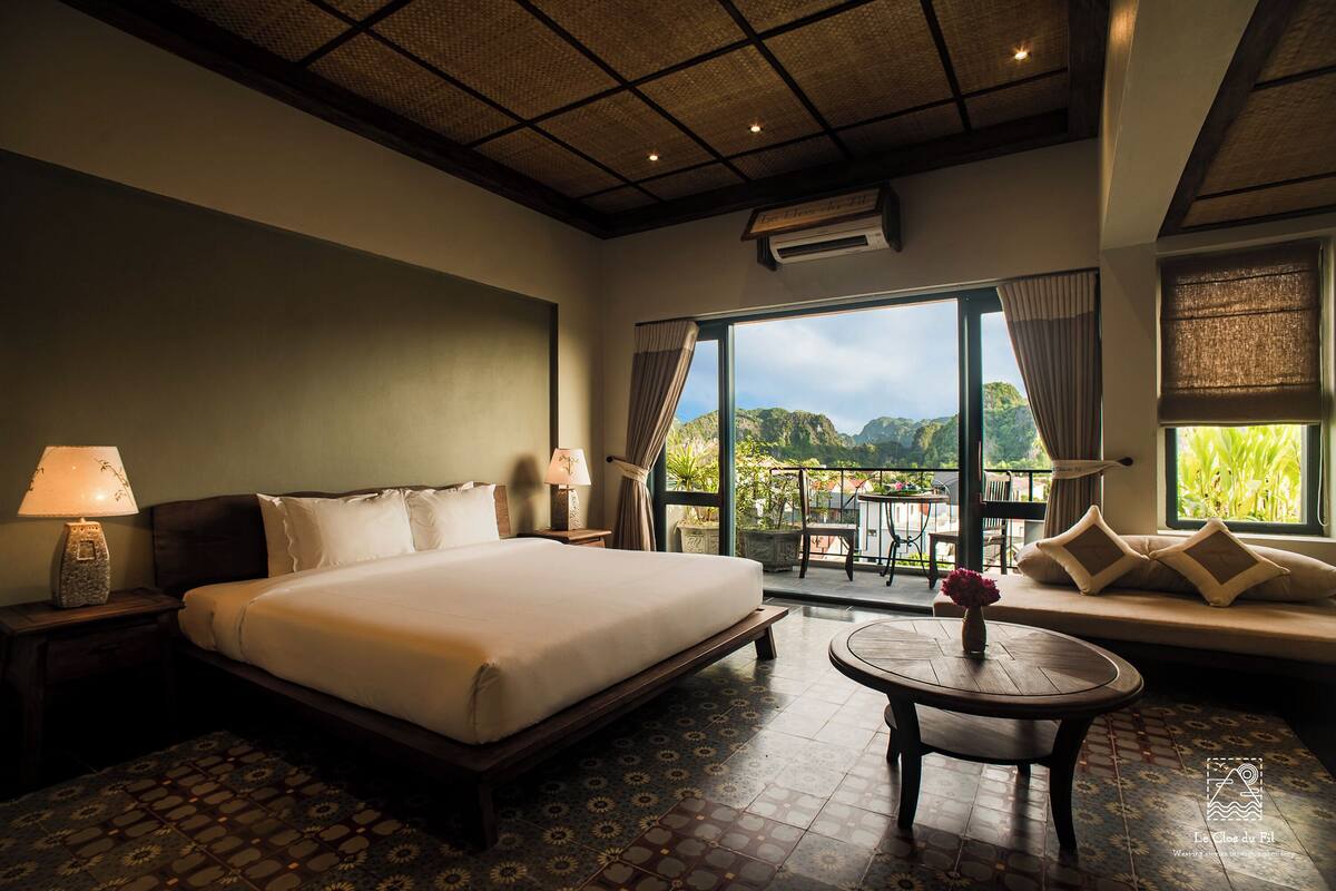 A hotel room with a large bed, a round table, and a view of the mountains through the windows.
