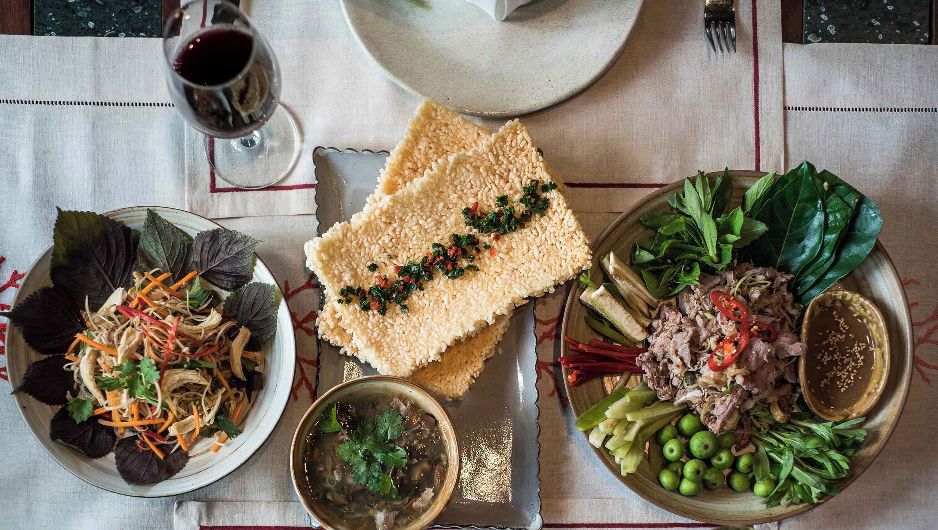 Een gedekte tafel met verschillende gerechten, waaronder een salade, soep en vlees, en glazen rode wijn.