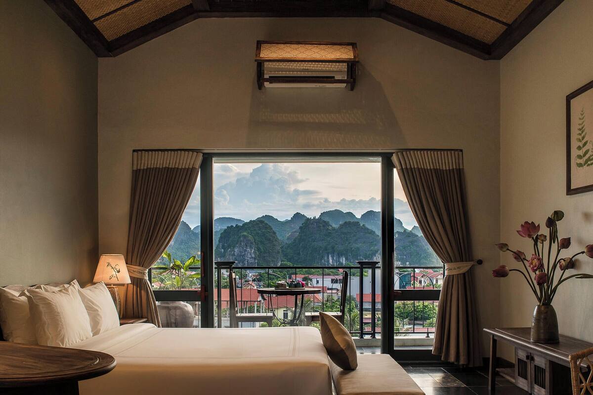 A bedroom with a large bed, a desk, a chair, and a view of mountains through a large window.