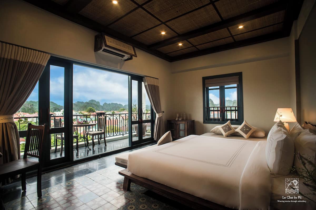 A bedroom with a large bed, a view of the outdoors, and a balcony with furniture.