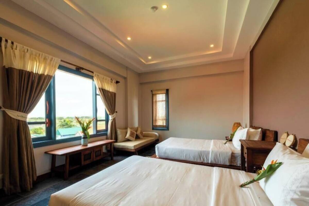A hotel room with two beds, a sofa, a small table, and a window with curtains.