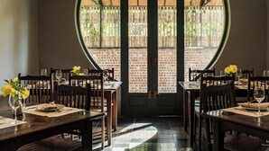 A dining area with a brick wall and a large circular window. Tables are set with plates, cutlery, and glasses. - Le Clos Du Fil (Nam Hoa Lu)
