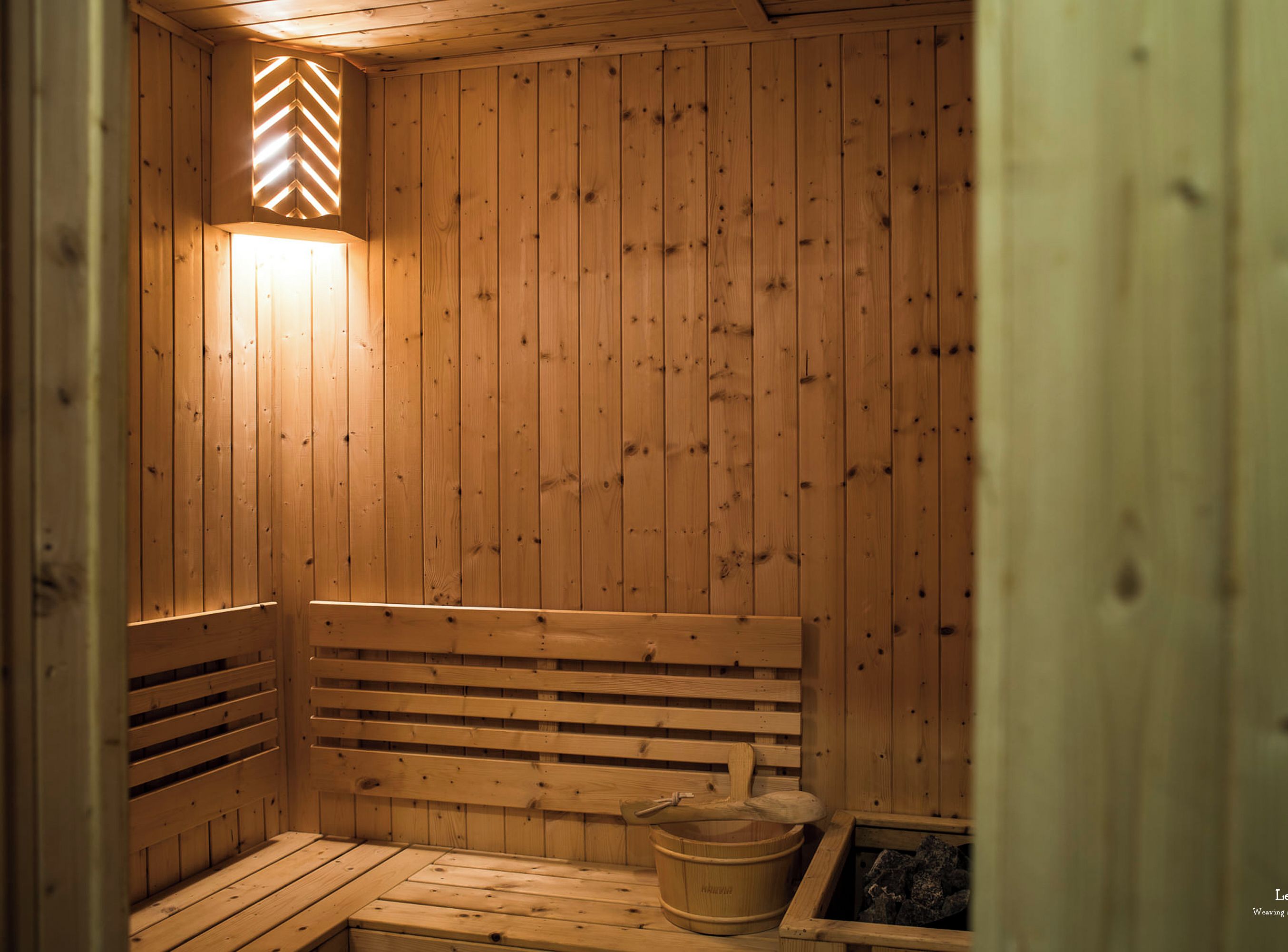 Una sauna de madera con bancos y una pila de piedra.