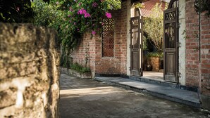 A brick building with a covered entrance, a stone wall, and flowering vines. - Le Clos Du Fil (Nam Hoa Lu)