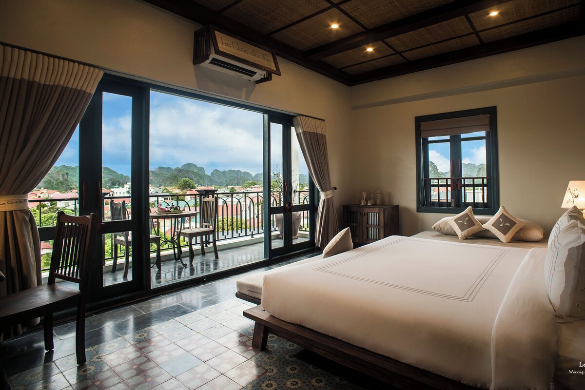 A bedroom with a large bed, a view of the outdoors, and a balcony with furniture.