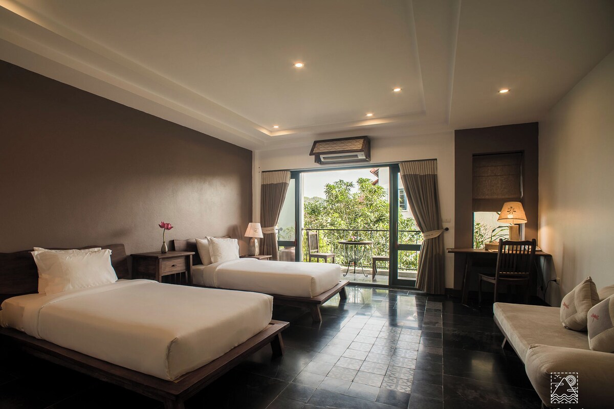 A hotel room with two beds, a balcony, and a desk with a chair.