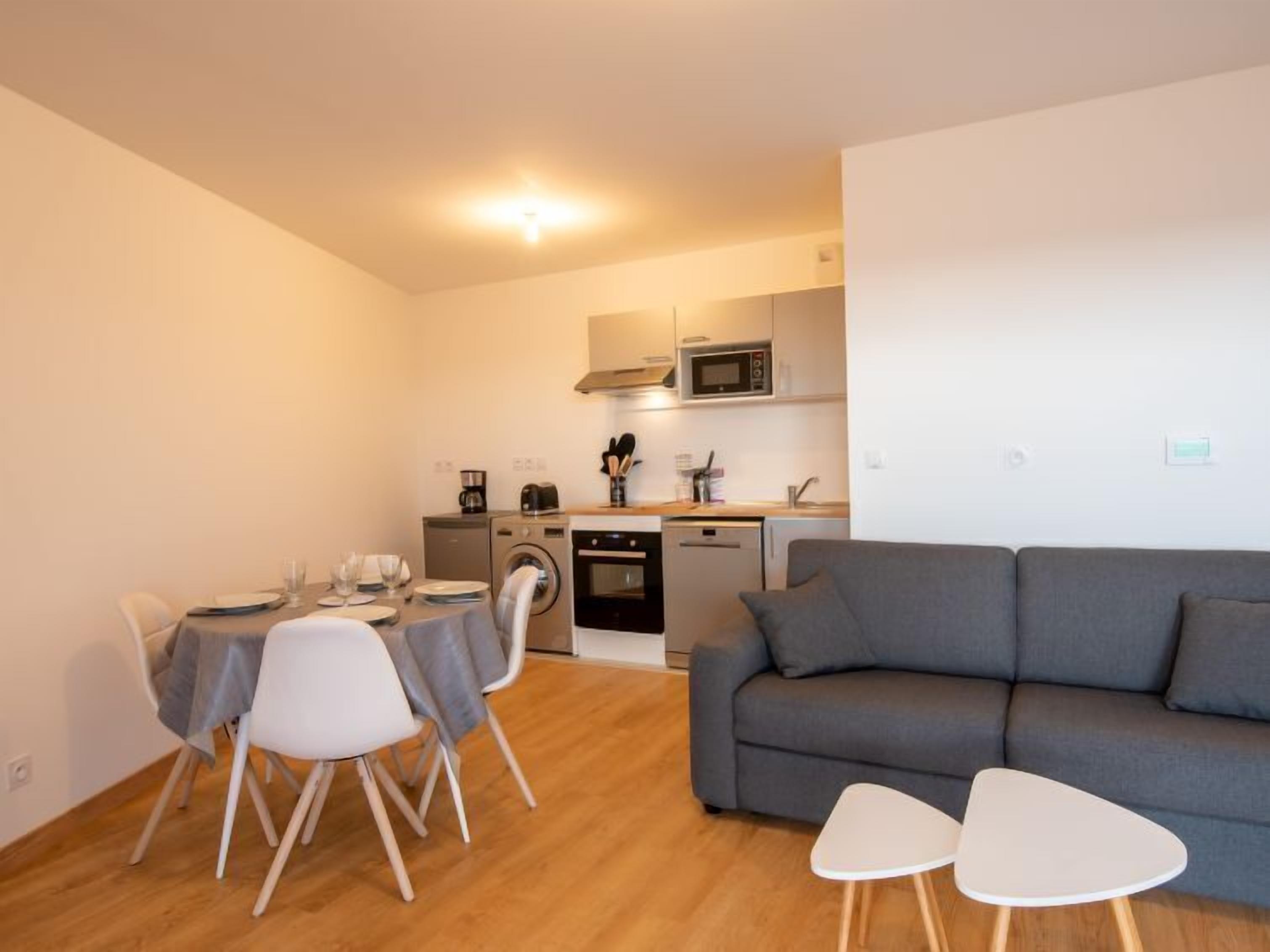 A compact living space with a dining area, a gray sofa, and a kitchenette.