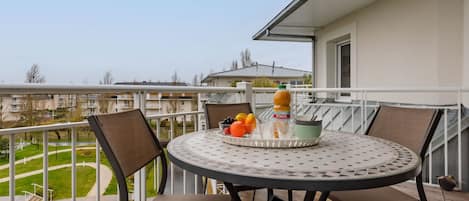 A balcony with a round table and four chairs, a bottle of Joker, and a fruit bowl.