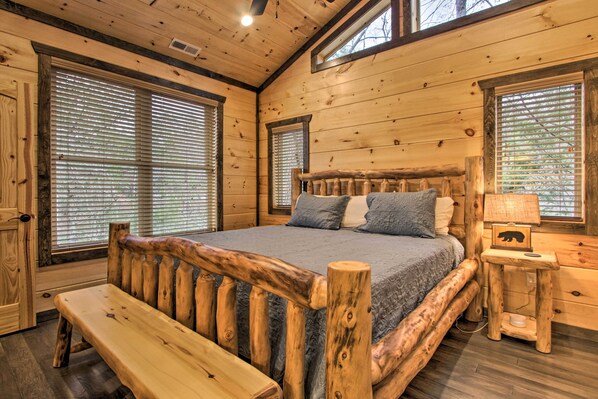 Une chambre dans une cabane en bois, avec un grand lit, un banc et une table de chevet avec une lampe.
