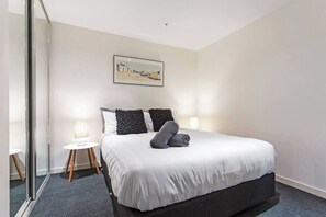 A hotel room with a bed, bedside lamps, a painting on the wall, and a small round table.